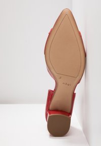 Escarpin en cuir verni rouge avec un bout pointu et une semelle texturée marron, mettant en avant un extérieur lisse et brillant et un petit talon carré.