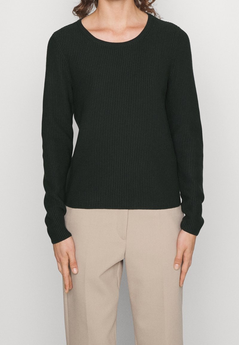 Maglione a maniche lunghe ribbed verde scuro con scollo rotondo, abbinato a pantaloni beige chiaro. Presenta una silhouette aderente e un tessuto testurizzato.