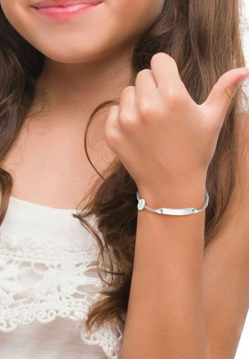 Pulsera de plata con una placa central alargada y lisa, unida por una cadena trenzada, llevada en una muñeca sobre un fondo de tela neutro.
