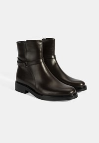Bottines en cuir marron foncé avec une texture lisse, dotées d'un détail de sangle et d'un petit talon épais pour plus de stabilité.