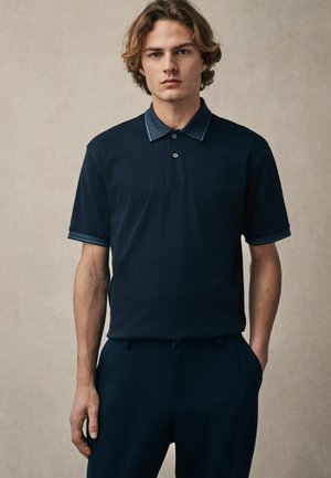 Navy polo shirt with a textured collar and detailed cuffs. Short sleeves and a button placket add to the design. Smooth cotton fabric.