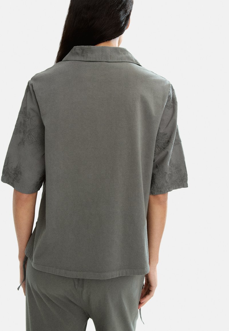 Camisa de manga corta en suave tela gris con bordados florales en las mangas, con un cuello clásico y un corte relajado.