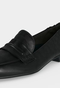 Μαύρο δερμάτινο loafers με μυτερή μύτη, χαμηλό χοντρό τακούνι και ραμμένη λεπτομέρεια λουριού πάνω στο πάνω μέρος.