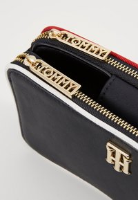 Black leather bag with gold zippers and “TOMMY” branding. Features red and white trim, and a textured surface. Zipper handle pulls visible.