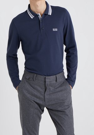 Marineblauwe polo met lange mouwen, voorzien van een twee-knopen placket, een contrasterende gestreepte kraag en grijze broeken met zijzakken en een relaxte pasvorm.