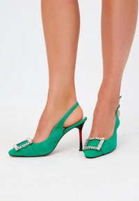 Grüne Wildleder-Slingback-Pumps mit spitzen Zehen und einer dekorativen Riemen-Schnalle aus Strass vorne. Mit einem rot getönten Stiletto-Absatz.