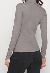 Langärmliges graues Turtleneck-Oberteil aus geripptem Stoff, figurbetontes Design, nahtlose Bündchen, leicht hoher Kragen, kombiniert mit dunklen Jeans.