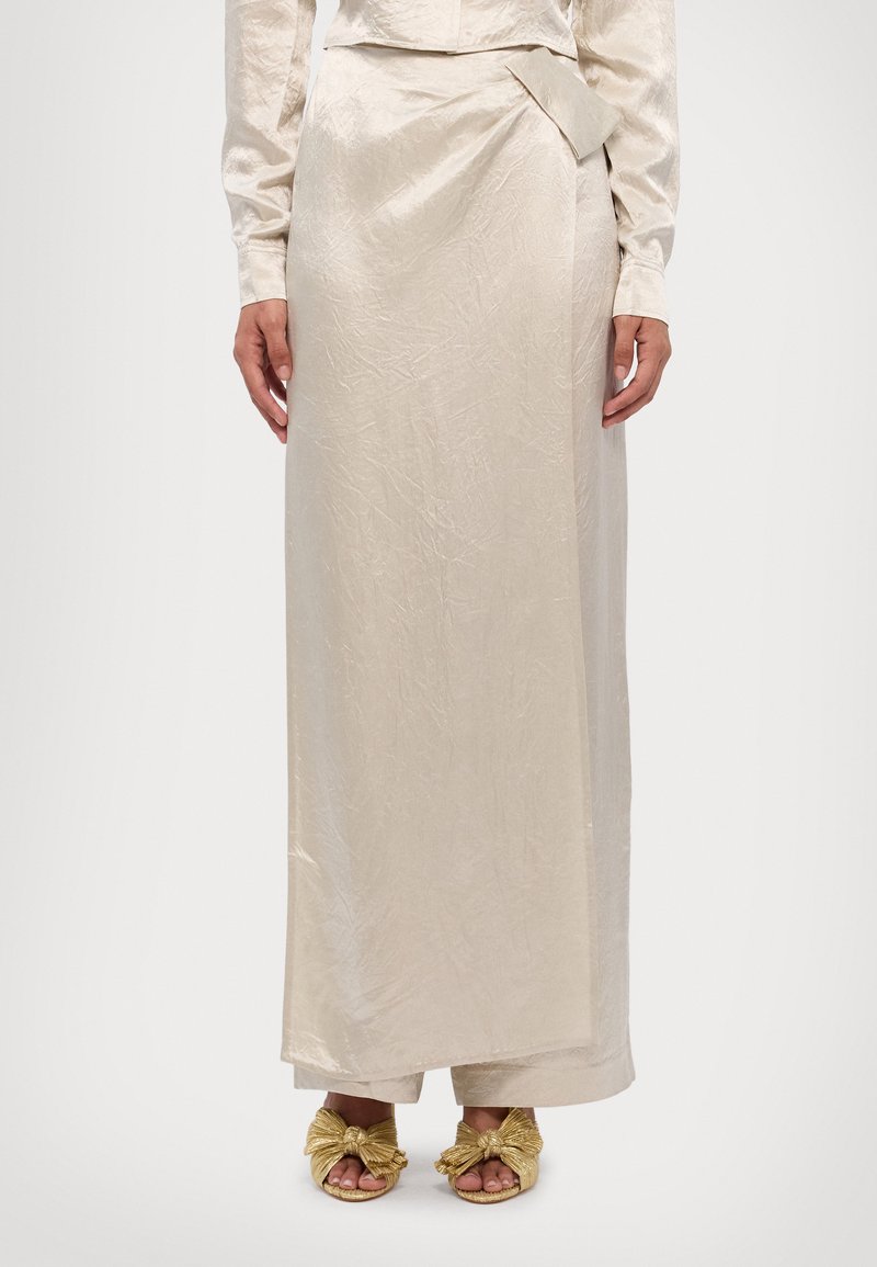 Beige satin midi skirt with a crinkled texture and a side pleat detail, paired with gold knotted sandals.