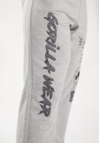 Grijze sweatpants met donkere grafische prints aan de zijkant, waaronder de tekst "GORILLA WEAR", gemaakt van een zacht, gestructureerd katoenmateriaal.