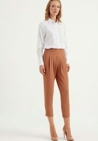 Lichtgewicht wit overhemd met lange mouwen, gecombineerd met bruine hoge taille broek met plooien en een zijritsdetail.