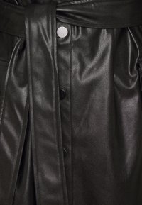 Czarna skórzana kurtka z paskiem w talii, gładką fakturą i zatrzaskami. Projekt zawiera fałdy, które nadają strukturę.