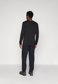 Black long-sleeve top with a round neckline, paired with dark pants and hiking shoes. The fabric appears soft, and the fit is relaxed.