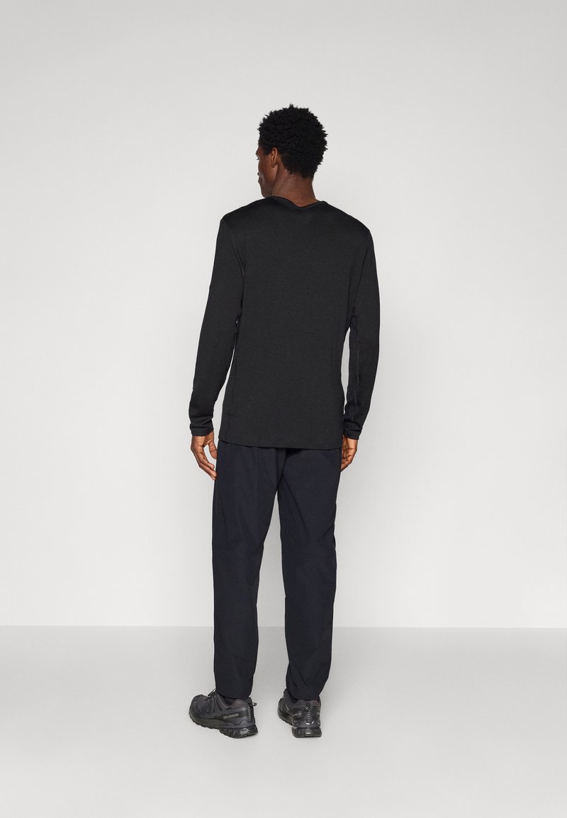 Black long-sleeve top with a round neckline, paired with dark pants and hiking shoes. The fabric appears soft, and the fit is relaxed.