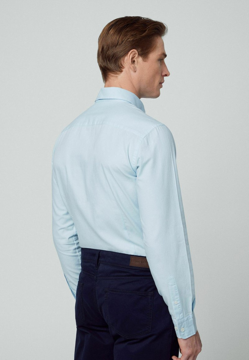 Helles blaues Langarmhemd mit Button-Down-Kragen, geradem Rücken und geknöpften Manschetten, kombiniert mit dunklen Hosen, die für eine genaue Passform entworfen wurden.
