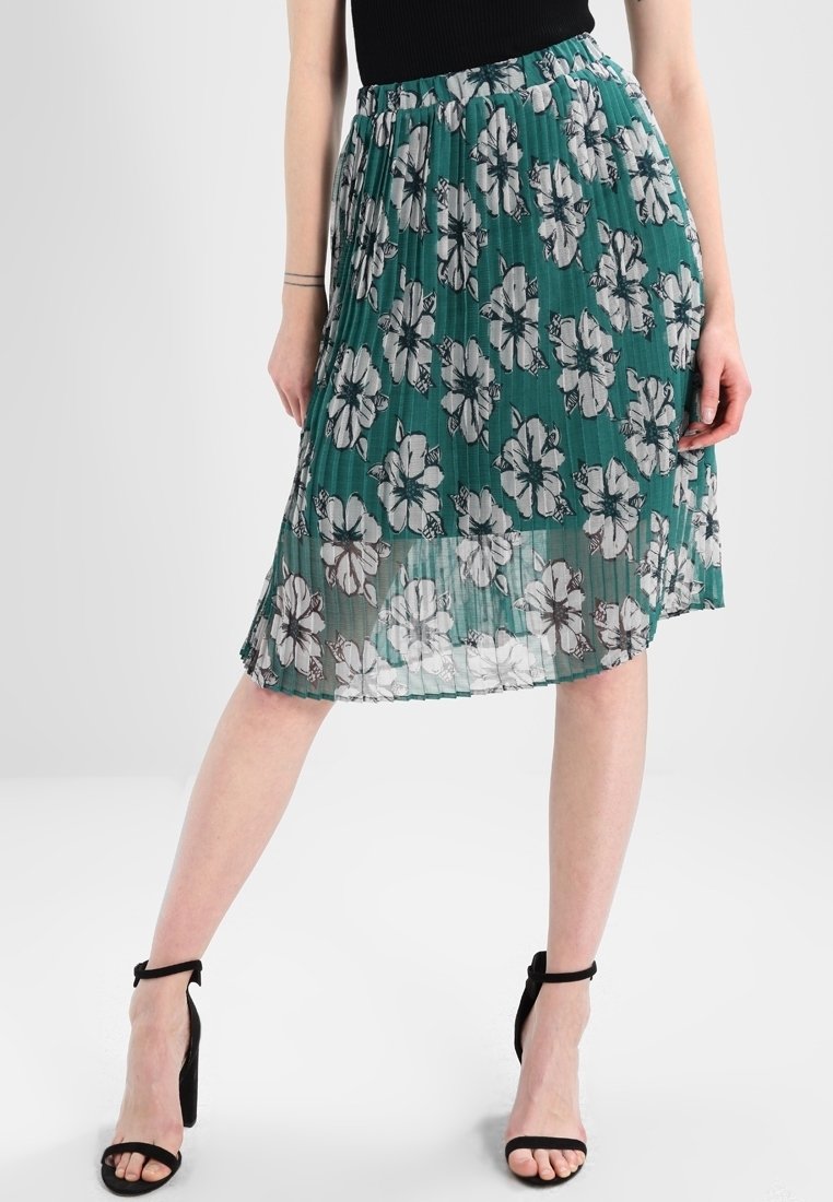 Gonna verde plissettata con motivo floreale bianco, dotata di una vita elastica e un tessuto leggero e semitrasparente.