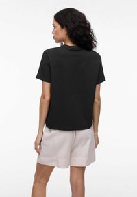 Svart t-shirt med kort ärm, avslappnad passform, rundad hals, tillverkad av mjukt tyg. Kombinerad med ljusbeiga shorts, minimalistisk design, inga synliga logotyper.