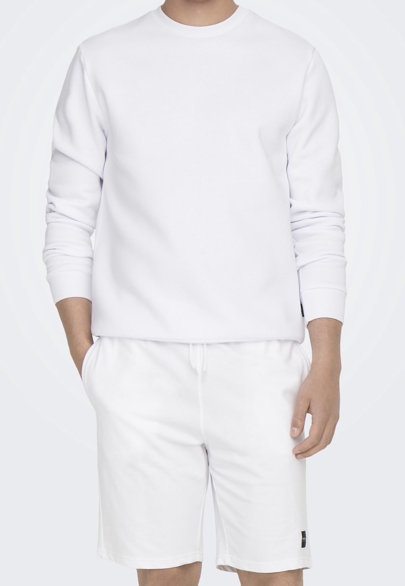 Sweat-shirt en coton blanc à manches longues avec poignets côtelés, associé à un short blanc équipé d'un cordon de serrage et d'une petite étiquette de marque.