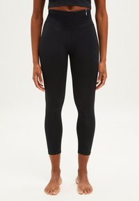 Leggings taille haute noirs avec une texture lisse, longueur cropped et détails de couture subtils, conçus pour la flexibilité et le mouvement.