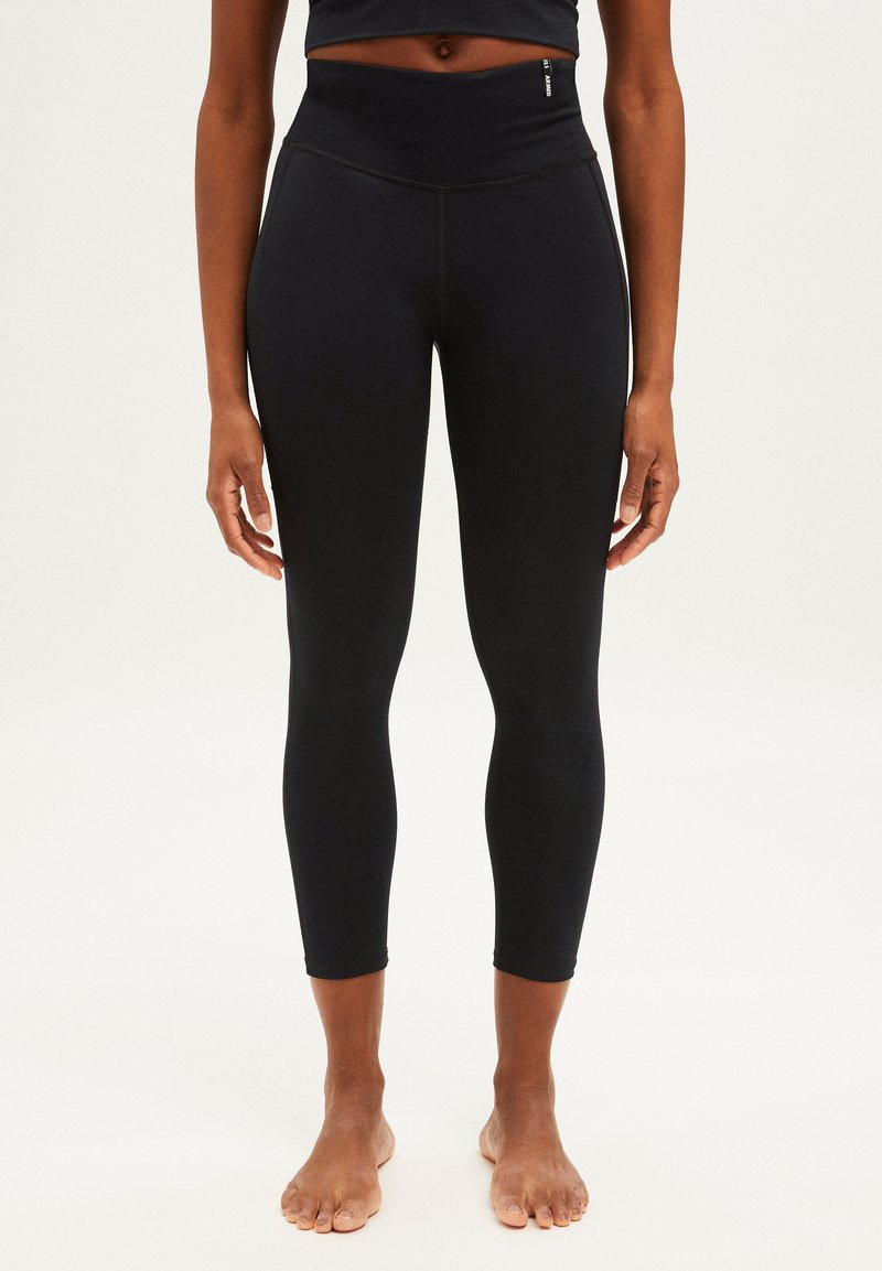 Leggings taille haute noirs avec une texture lisse, longueur cropped et détails de couture subtils, conçus pour la flexibilité et le mouvement.