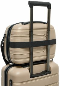 Beige harde koffer met een verlengd zwart telescopisch handvat, een kleinere bijpassende koffer bevestigd met een horizontale zwarte riem.