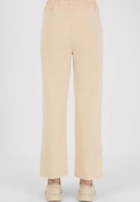 Beige wide-leg pants with an elastic waistband and smooth texture, paired with light-colored sneakers, seen from the back.