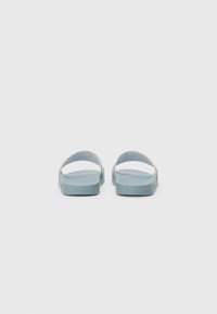 Blå sandaler med flat såle, åpen bak og to buede stropper. Teksturert materiale og minimalistisk design. Ingen ekstra feste eller mønstre.