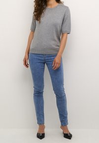 Šedý pletený svetr s krátkým rukávem a kulatým výstřihem, zkombinovaný se světle modrými skinny džíny. Černé lodičky s špičatou špičkou dokončují celý outfit.