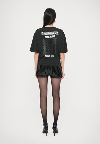 Black oversized t-shirt with white graphic text on the back, paired with shiny black shorts and black tights, completed with high heels.