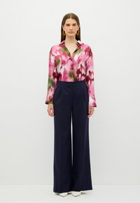Långärmad skjorta i rosa och grön blommig mönster med knappar, kombinerad med vida navy-byxor och vita spetsiga skor.