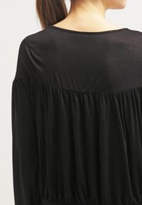 Svart tygtröja med lös passform. Har en bred halsringning och samlad textur på baksidan. Tillverkad av ett mjukt, lätt material.