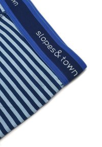 Tessuto a righe blu e azzurro con una ampia vita elastica blu scuro che presenta il testo "slopes & town" in bianco.