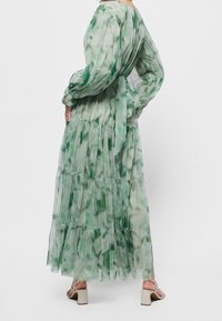 Long, tiered dress in sheer fabric featuring a green watercolor pattern. Elasticized sleeves, back tie, and ankle-length hem.
