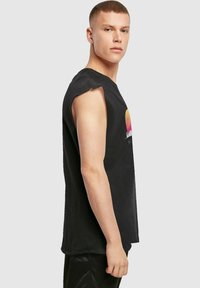 Tricou fără mâneci din bumbac negru, cu un design grafic colorat de apus pe față, cu margini brutale și o croială lejeră.