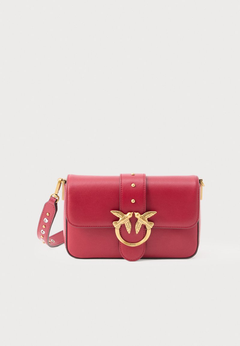 Red leather shoulder bag with a gold swallow motif clasp, silver studs on the strap, and a structured rectangular shape.