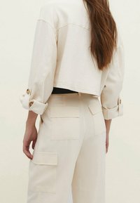 Beige cropped jakke med knappede manchetter og matchende højtaljede bukser med påsyede lommer, lavet af tekstureret stof.