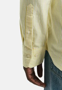 Geel gestreept shirt met witte strepen, voorzien van een doorgeknoopte manchetten en een puntzakdetail. Zachte stof met een comfortabele pasvorm.