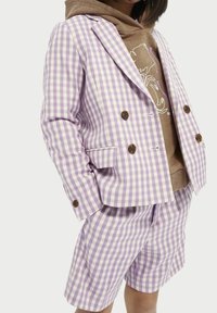 Lila ginghamrutad blazer med dubbelknäppt design, i kombination med matchande shorts. Underneath en brun hoodie med grafiskt tryck.