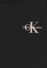 Černé bavlněné tričko s kulatým výstřihem, na přední straně bílé a růžové logo "Calvin Klein Jeans" se stylizovaným grafikou "CK".