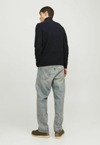 Marineblauer Strickpullover mit hohem Kragen, kombiniert mit hellblauen, weiten Jeans und braunen Schnürstiefeln. Schlichte Textur und keine sichtbaren Muster.