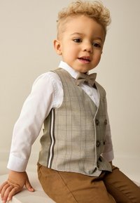 Un gilet à carreaux gris sur une chemise blanche, avec un nœud papillon et un pantalon marron. Le gilet a des boutons doubles et des accents rayés.