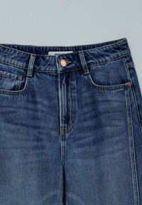 Dark blue denim jeans with a straight cut, featuring copper button hardware, front pockets, and visible stitching details.