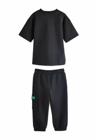 Sort kortærmet t-shirt med rund hals, kombineret med sorte sweatpants med elastisk talje og en sidelomme med grønne bogstaver.