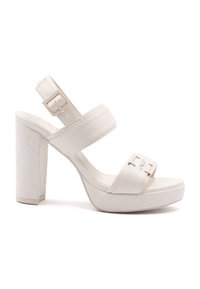 Valkoinen platform-korkokenkä, jossa on kaksi leveää hihnaa, säädettävä nilkkaketju ja tekstuuri pohjassa, jossa on kohokuvioituja kuvioita.