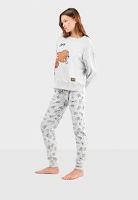 Sweatshirt gris avec un personnage de dessin animé affichant une expression ludique, associé à un pantalon de pyjama gris clair ornés d'un motif de dessin animé répétitif.