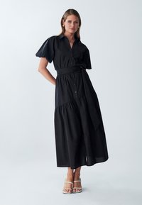 Abito nero con bottoni, maniche a palloncino corte, vita definita legata con una cintura e una gonna fluida con design a strati.