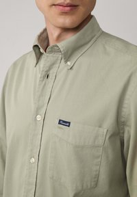 Camicia button-up verde chiaro con colletto classico, dotata di taschino sul petto e di un'etichetta con logo, realizzata in morbido tessuto di cotone.