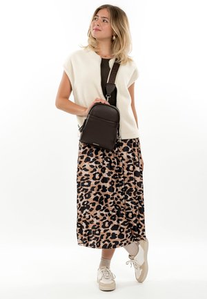 Sieviete valkā baltu vestīti, melnu topu, leoparda raksta svārkus, baltas kedas, bēšas zeķes un nēsā melnu šķērsroku somu.