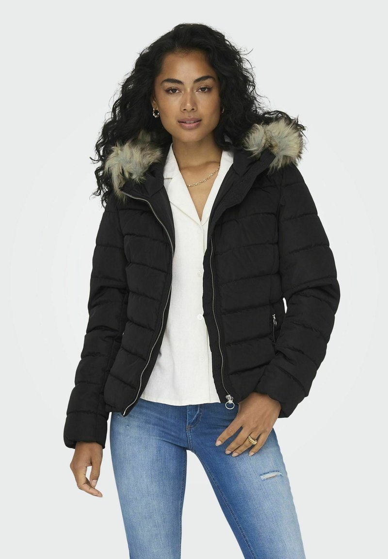 Sorte puffer-jakke med hette med pelskant, glidelås og quiltet design. Brukes over en hvit skjorte og blå jeans, med sidelommer.