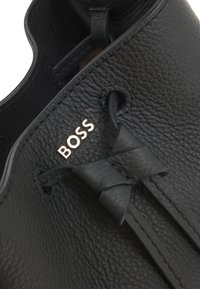 Mustast nahast king, millel on tekstuuriga pind, lipsukujuline pael detail ning metallist "BOSS" logo. Lähedal kaader, kus on nähtavad õmblused.