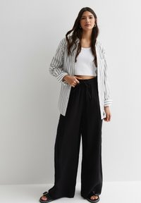 Zwarte wijd-uitlopende broek met elastische tailleband, gecombineerd met een witte crop top en een gestreepte lange mouwen shirt. Glad stof en casual ontwerp.